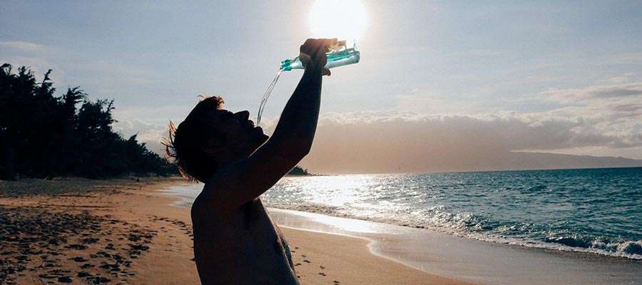 homem bebendo água na praia